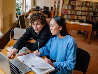 Two students working together at a laptop in a library